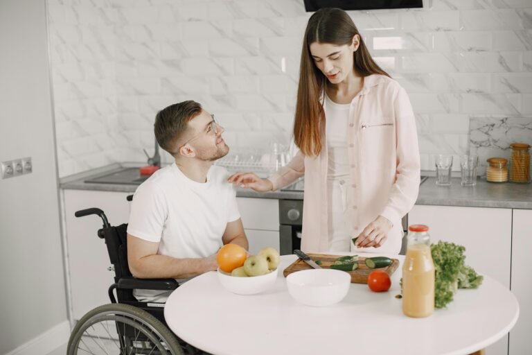 A man in a wheelchair and a woman preparing food together in a modern kitchen.
