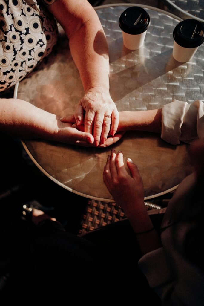 Two women sharing a heartfelt moment, holding hands over coffee in a warm setting.